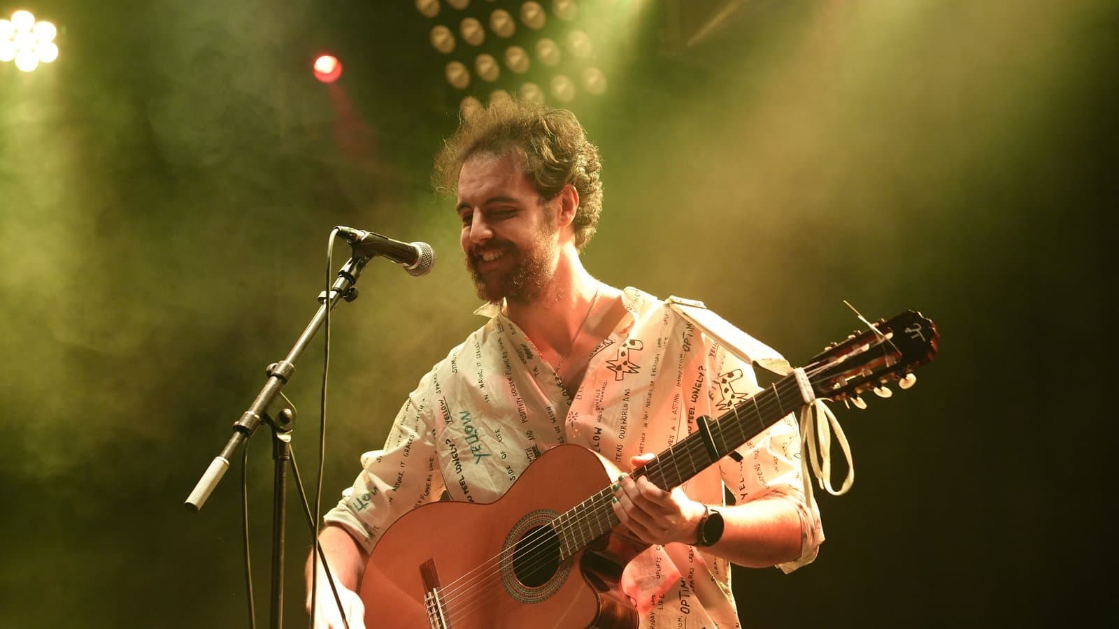 Musician smiling while playing acoustic guitar on stage