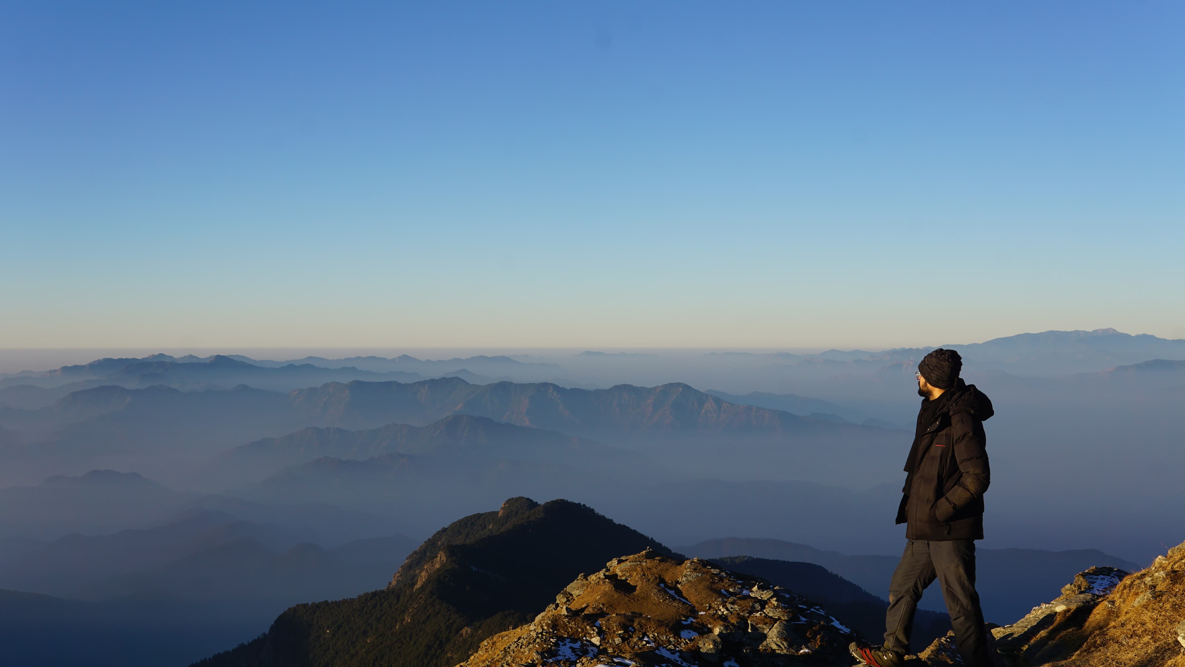 Hiker standing on a mountain summit overlooking misty ridges at golden hour