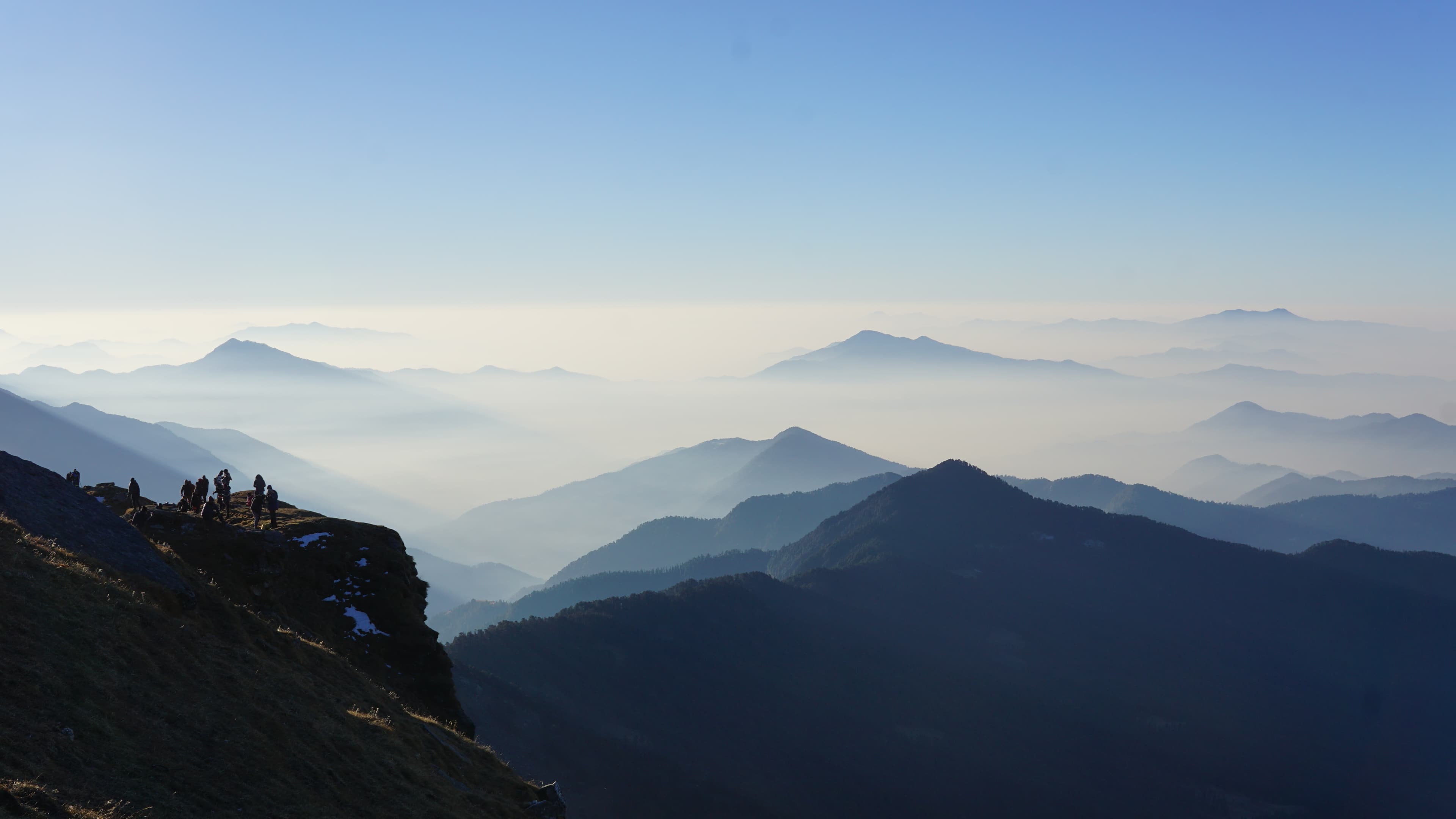 Hikers standing on a cliff edge overlooking layered misty mountain ridges at dawn