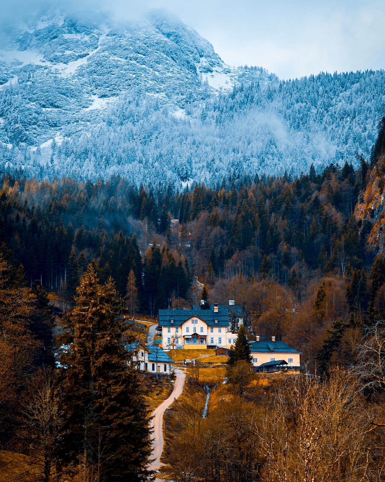A countryside estate surrounded by autumn trees beneath frost-covered alpine peaks