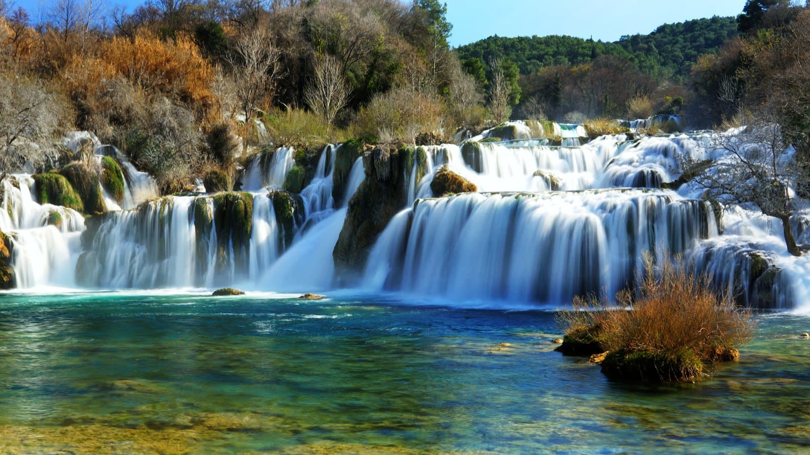Turquoise terraced waterfalls cascading over mossy rocks in sunlight