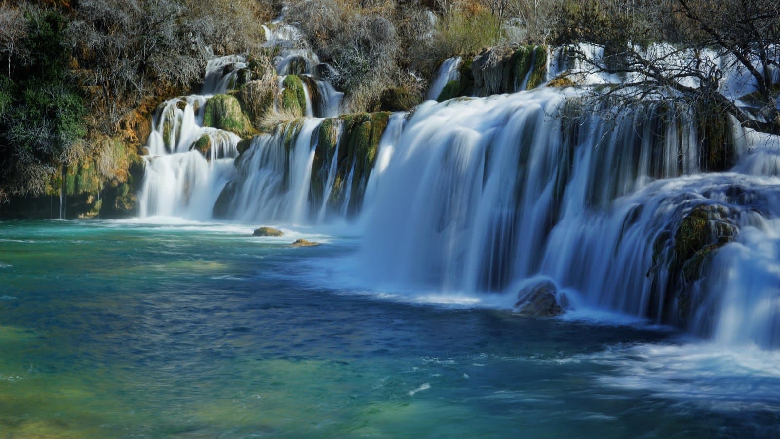 Silky smooth waterfall flowing over emerald rocks into crystal clear pool