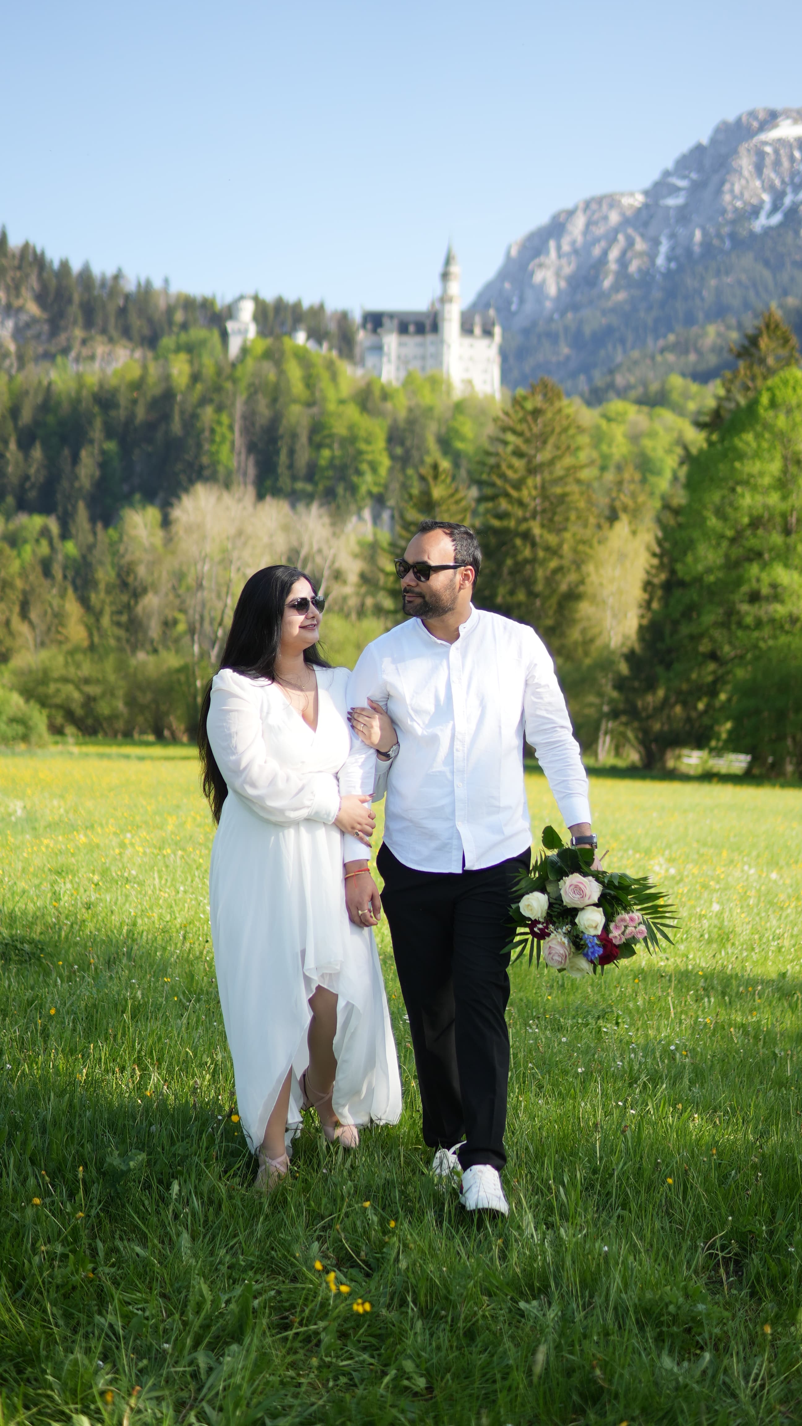 Bride and groom sharing a tender moment in a lush green meadow with mountains in the background