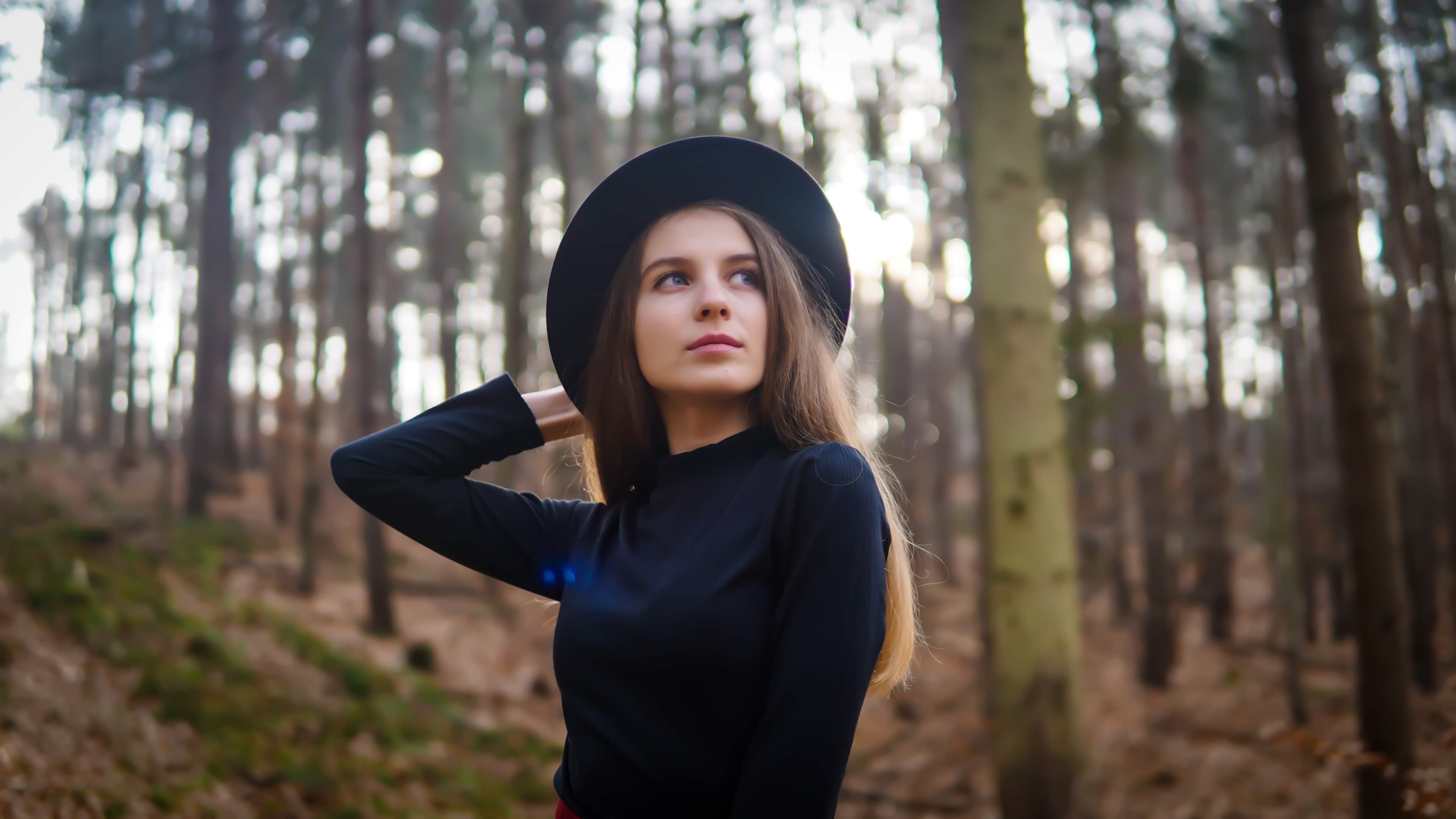 Young woman in a black hat and sweater looking upward in a misty autumn forest