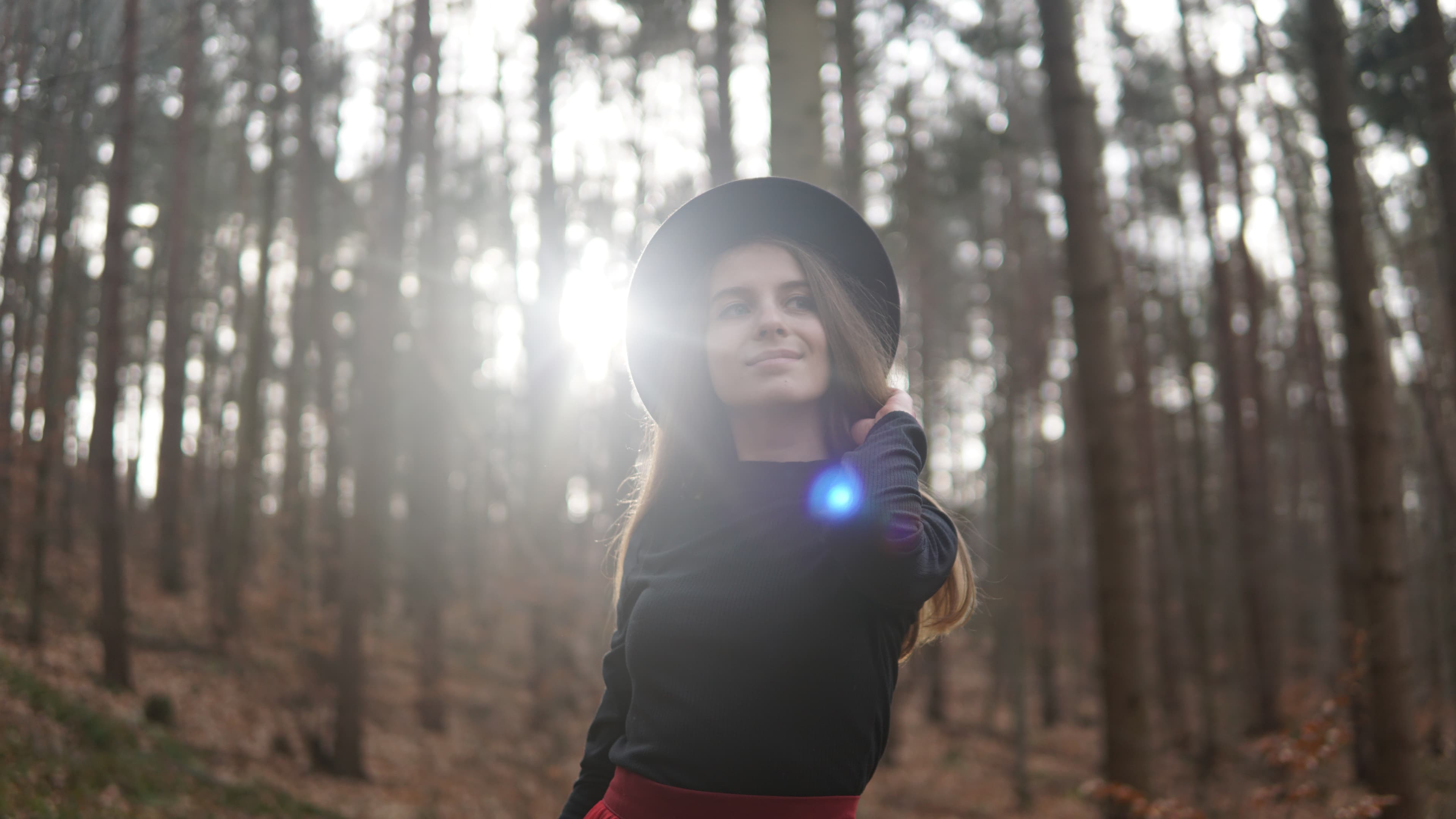 Woman smiling softly with sun flare streaming through bare forest trees behind her