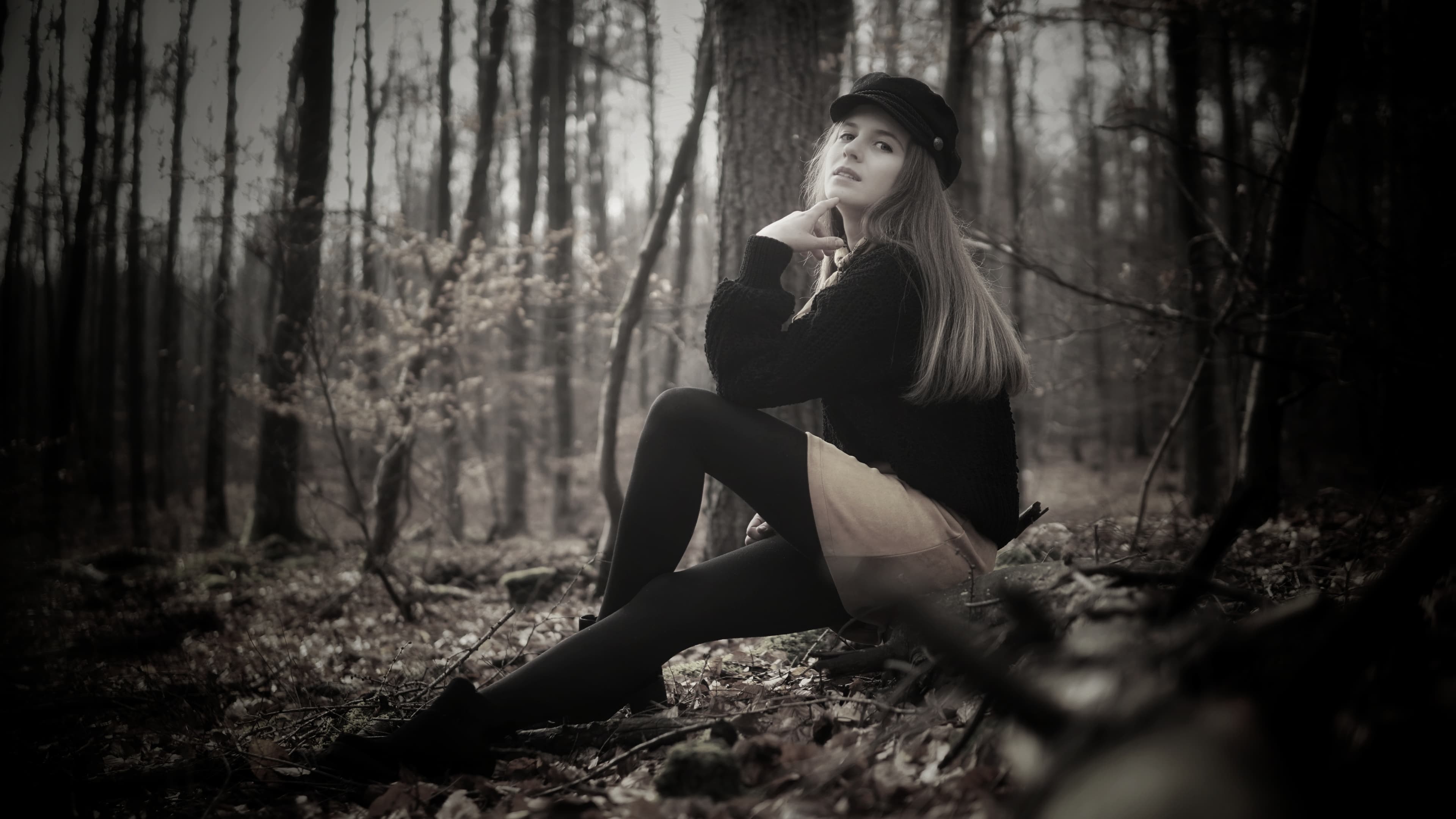 Desaturated portrait of a woman seated on the forest floor gazing pensively into the distance