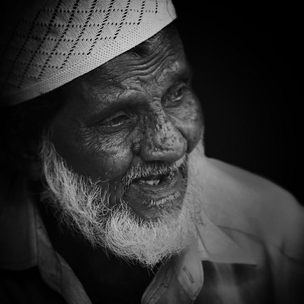 Black and white close-up portrait of an elderly man with a white cap and textured beard