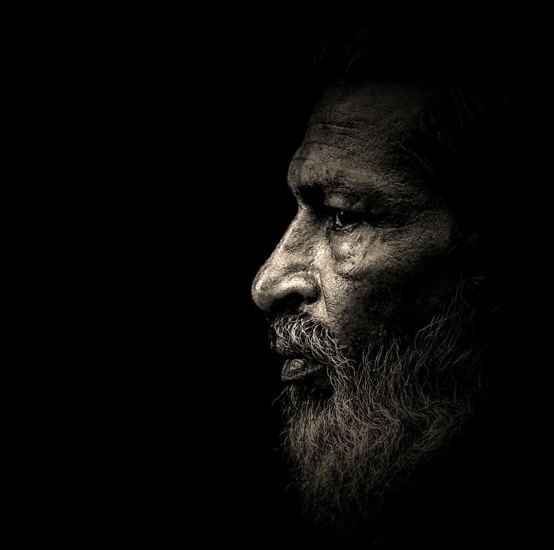 Dramatic black and white side profile of a bearded man emerging from darkness
